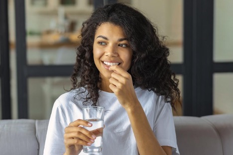 A woman takes prescribed medication for bowel preparation holding a glass of water and medicine