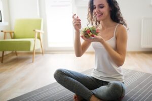 A woman sits on the floor eating vegetables and fruits to improve her health and digestive system